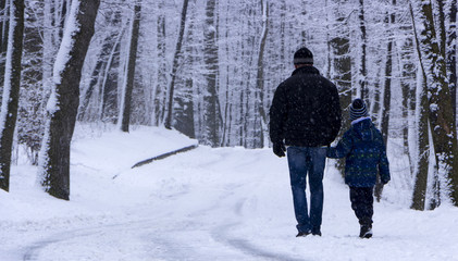 A man with his son is walking in a snow-covered forest