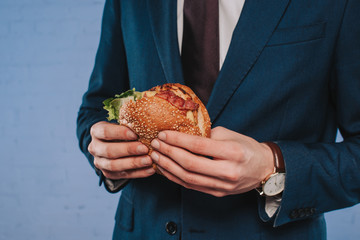 cropped shot of businessman in suit holding burger