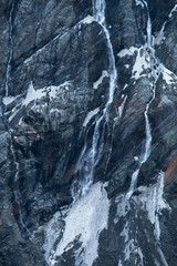 Fototapeta na wymiar Black tall cliff with ice and waterfall begining of the glacier in Mt Cook National Park.