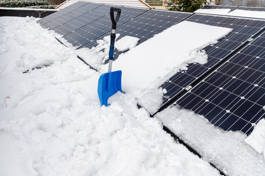Photovoltaic panels on the roof with snow, with a snow shovel in the winter