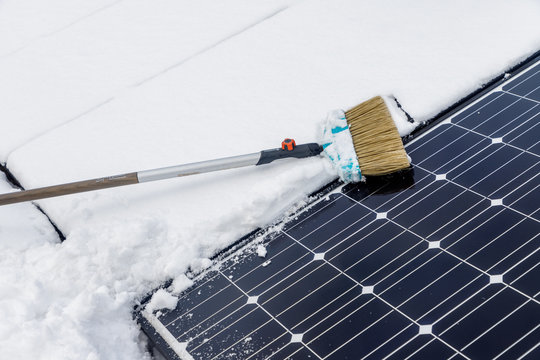 Photovoltaic panels on the roof cover with snow, with a bass-broom in the winter