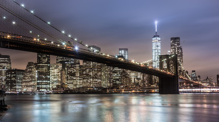Panele Szklane  Brooklyn bridge i New York City Manhattan skyline o zmierzchu z oświetlonymi drapaczami chmur nad panoramą East River.