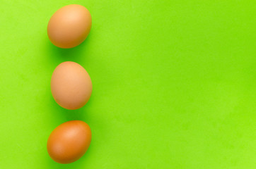 Three brown eggs on bright light green background