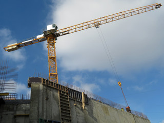 Crane on the construction site against the cloudy blue sky