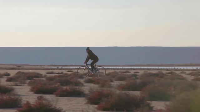 Man cycling at the lake bank in wasteland at sunset in autumn time