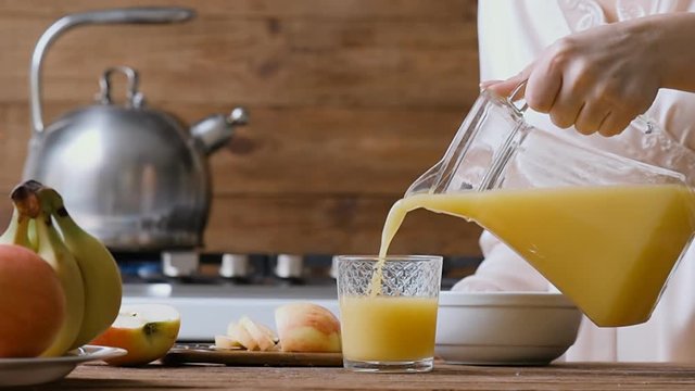 Young woman pouring the orange juice into a glass. Breakfast. 