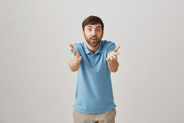 Fototapeta premium Impressed excited european worker gesturing towards camera as if talking about person, being amazed and happy while standing over gray background. Guy congratulate friend that did something great