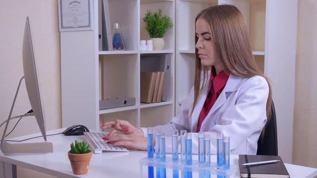 young professional medical scientist working in the office. woman wearing uniform white lab coat. entering the results of the experiment to the computer