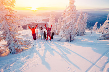 Group of snowboarders friends meet the dawn in mountains. They raised their arms up, they were...