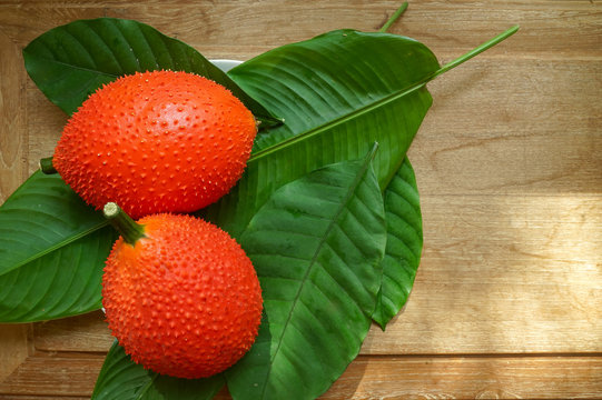 Two Gac fruits (Momordica cochinchinensis) on green leaves placing on golden teak table