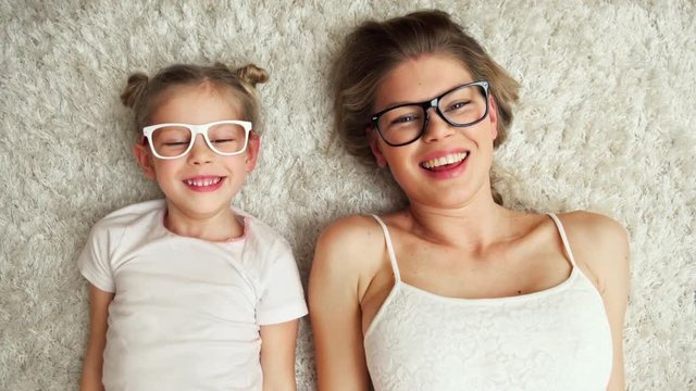 Happy laughing family putting on optical glasses lying on carpet at home. Vision and eye care concept. 
