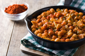 Fried spicy chickpeas in frying pan on wooden table