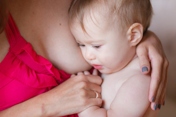 Upset baby near woman's breast. Refusing breastfeeding
