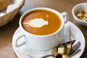 Tomato puree soup with cream and crackers in a white plate on the table