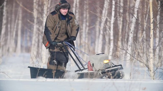 Man overcoming deep snow on a mini snowmobile in the snowy forest, skillful maneuvering