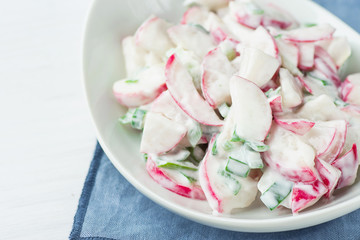 Healthy Red Radish and Green Scallion Onions Salad with Greek Yogurt Dressing in White Serving Bowl Standing on Blue Napkin. Easter Brunch Meal Spring Menu.