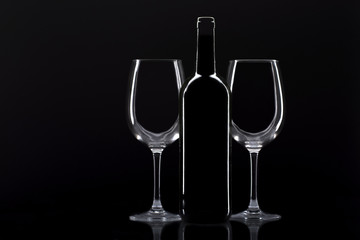 two glasses of wine and bottle of wine in front of said glasses on black background