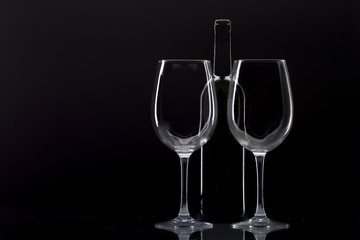 two wine glasses and bottle of wine behind said glasses on black background