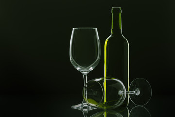 two wine glasses, one of them lying down and bottle of wine with green reflections with black background