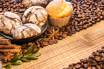 On a wooden table a mug of black coffee next to a plate of chocolate cookies sprinkled with powdered sugar, and on the background coffee beans spread with cinnamon, puddings and green coffee twing