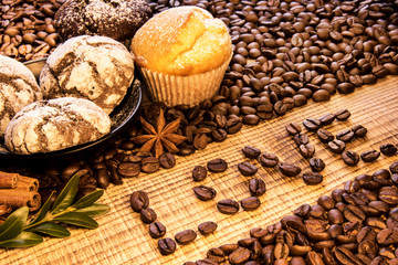 Inscription love on a wooden table with plate of chocolate cookies sprinkled with powdered sugar, and on the background coffee beans spread with cinnamon, puddings and green coffee twing