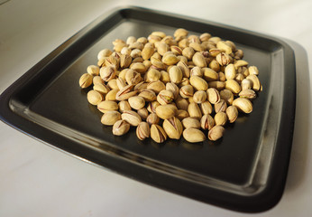 Pistachio nuts, a bunch on a black plate. A close-up photograph. Unrefined whole kernel 