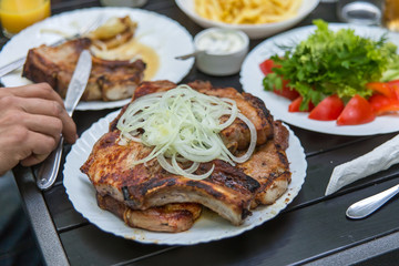 Fried pork steaks, cutlets with bones with onions, on a wooden table. A man's hand holds a knife