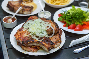 Fried pork steaks, cutlets with bones with onions, on a wooden table. A man's hand holds a knife