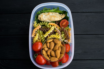 Lunch witn chicken and pasta  in the box on the black wooden background