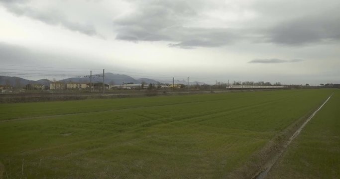 Treno alta velocit&agrave; che passa dal prato con un cielo nuvoloso