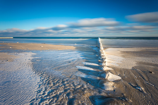 Winter landscape at the sea. Frozen wooden breakwaters line at Baltic Sea.