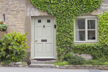 Fototapeta premium Wooden doors to a charming lime stone cottage surrounded by climbing ivy plant and shrubs .