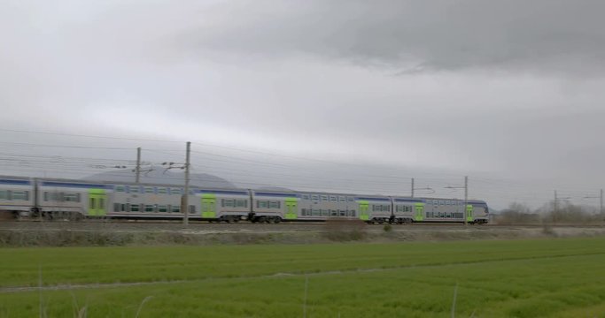 Treno passeggeri a due piani in transito in un prato verde con un cielo nuvoloso