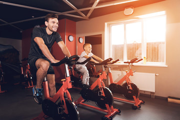 Fototapeta na wymiar Father and son in the gym. A man and a son are engaged in exercise bikes together.
