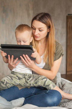 Young mother helping her son with digital tablet at home. Education and Technology