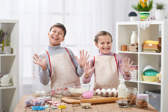 Child girl and boy cooking in home kitchen, showing hands with flour.