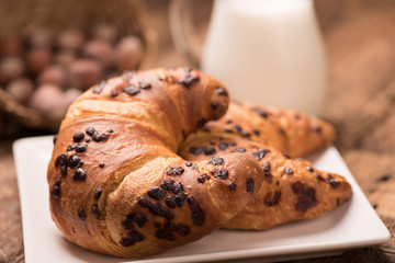 Fresh croissant on a wooden board  with milk. Freshly baked croissant on a dark wooden table.