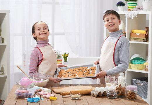 Boy and girl shows a tray of baked cookies in home kitchen interior, homemade food concept