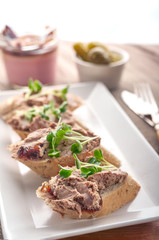 Liver pate spread on bread slices with greens and condiments.