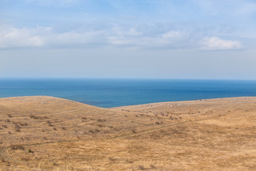 Fototapeta na wymiar Hilly seashore and a blue surface of the sea.