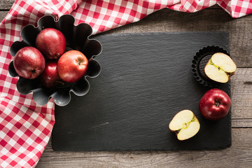 Ripe red apples on wooden board with red checkered towel. Copy space for text on dish from black slate.