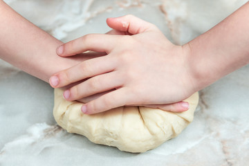 Children hands knead the dough on the table, closeup