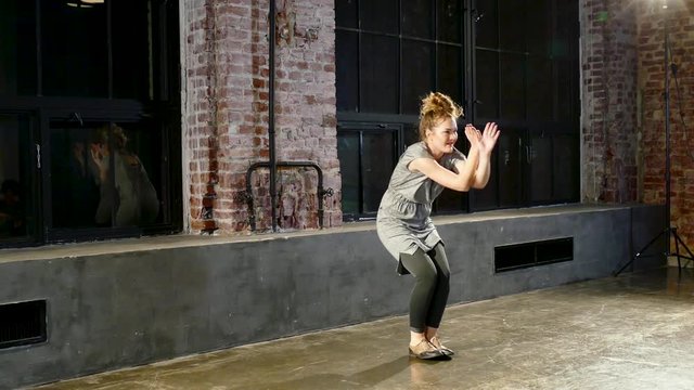 Young blonde woman performs in grey clothes near big window in studio. Modern dance.
