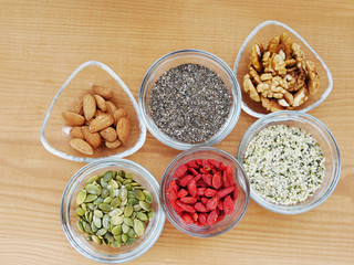 Superfood seeds, nuts and berries, chia, almond, walnut, hemp, pumpkin in glass bowl over wooden table