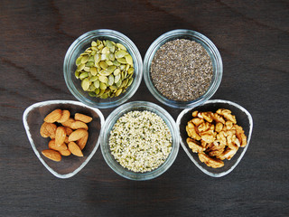 Five superfood seeds and nuts chia, almond, walnut, hemp, pumpkin in glass bowl over dark wooden...