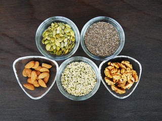 Five superfood seeds and nuts chia, almond, walnut, hemp, pumpkin in glass bowl over dark wooden table