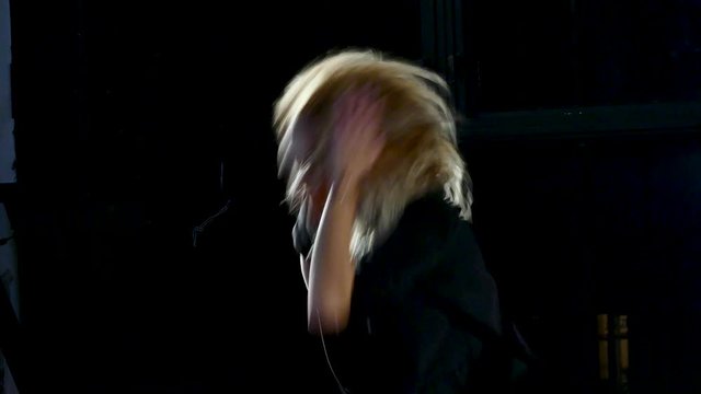 Young blonde woman performs in grey clothes near wall. Modern dance.
