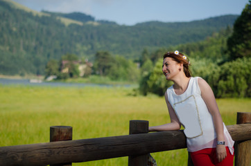young woman with long hair leaning against wooden handrails, red pants, white shirt, with flower crown in her hair. On a glorious spring day,