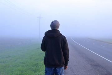 Man walking on a rural roadway covered with fog