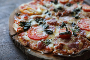 Pizza bacon ham tomato and cheese on top on wood background vintage style
